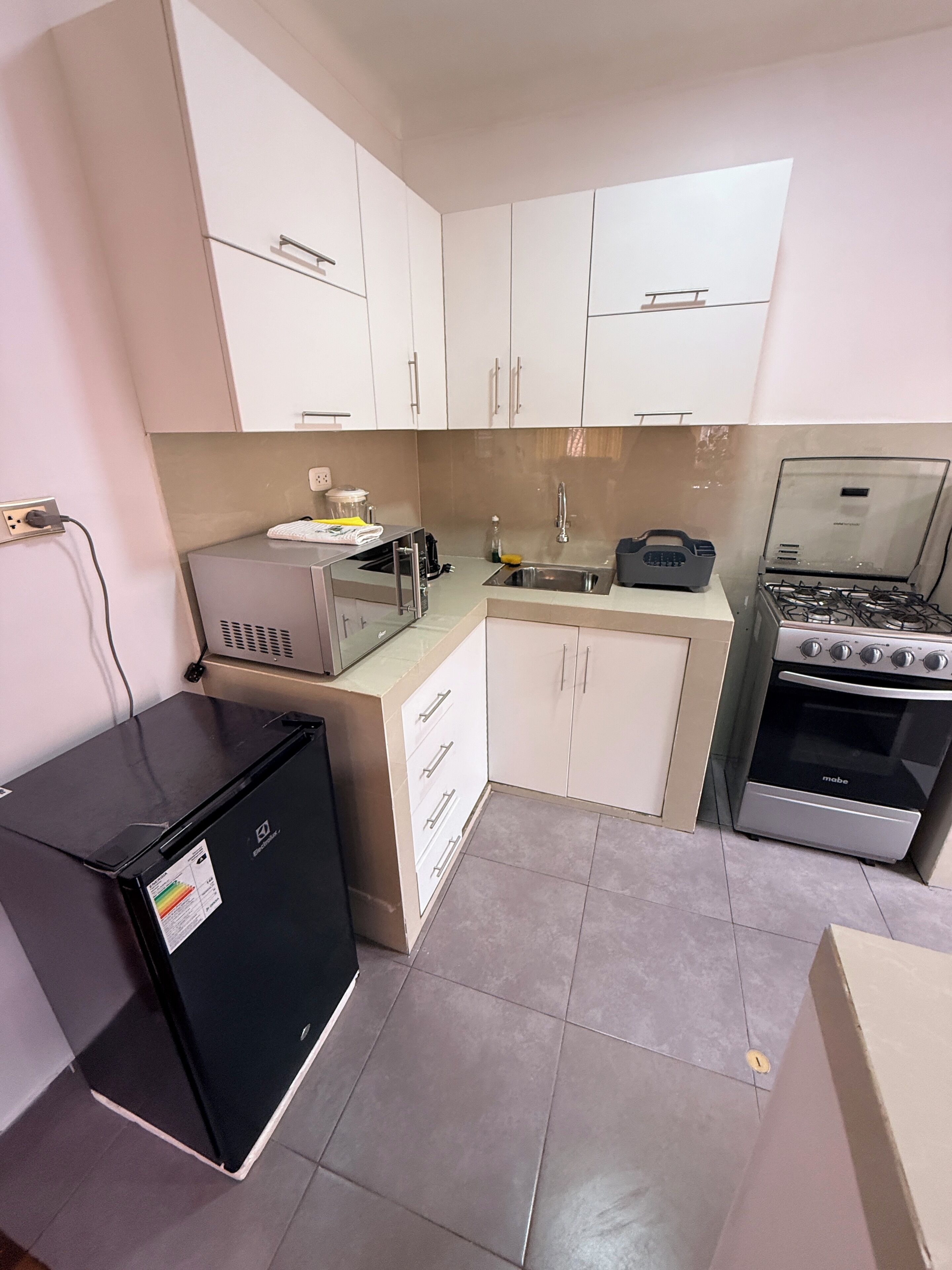 A compact kitchen with white cabinets, a black refrigerator, a gas stove, and a microwave.