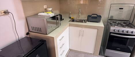 A compact kitchen with white cabinets, a black refrigerator, a gas stove, and a microwave.