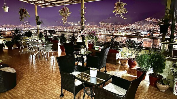 A restaurant with a city view, wooden floors, and black wicker chairs. - Hotel Inkasabios Cusco (Cusco)