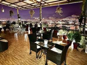 A restaurant with a city view, wooden floors, and black wicker chairs. - Hotel Inkasabios Cusco (Cusco)