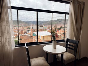 A room with a large window, a small round table, two chairs, and a vase with flowers.