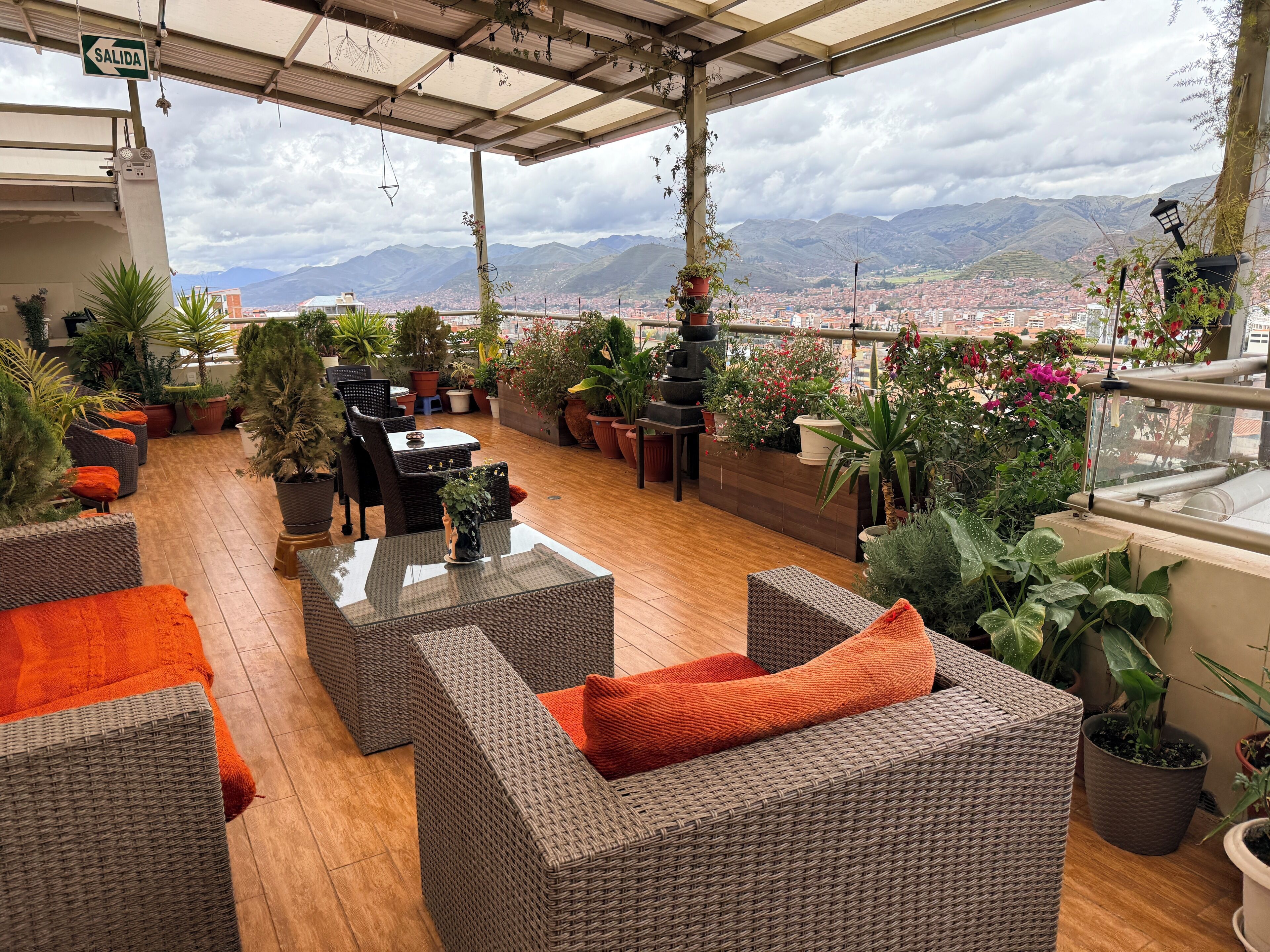 A covered outdoor seating area with wicker furniture, potted plants, and a city view.