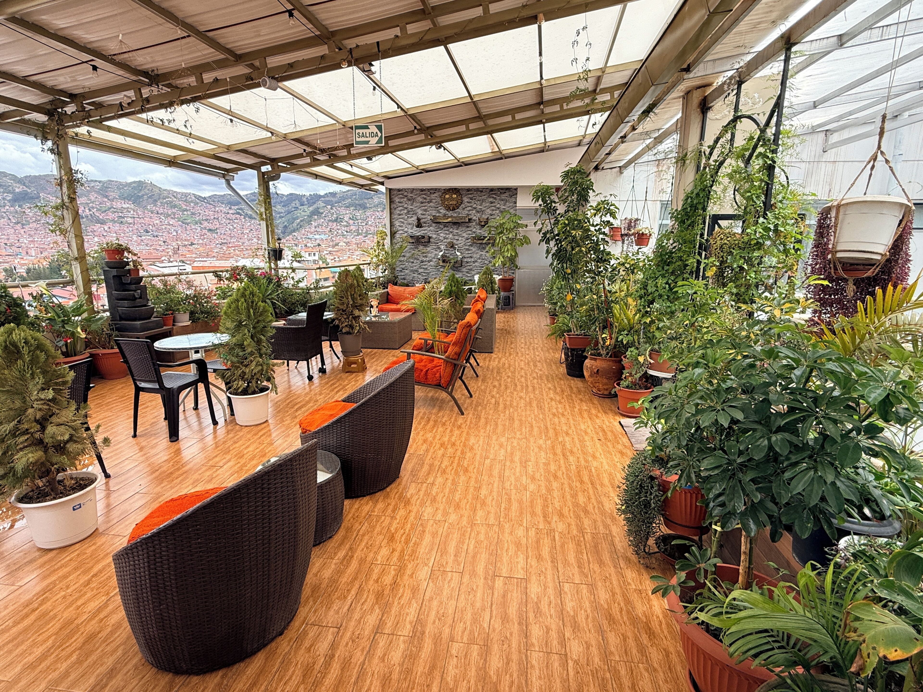 A covered patio with seating, potted plants, and a view of a cityscape.