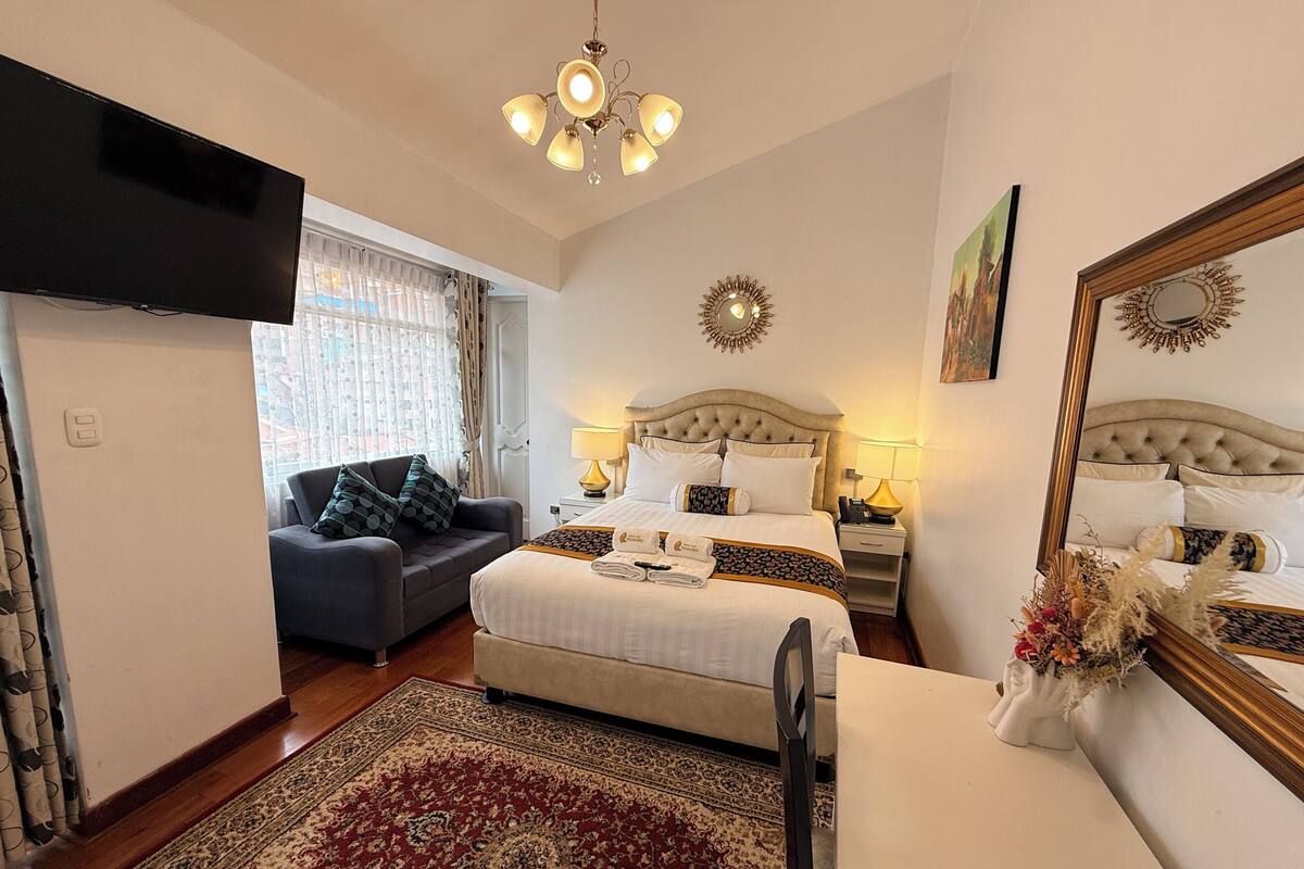 A hotel room with a bed, a sofa, a desk, a TV, a chandelier, and a mirror.