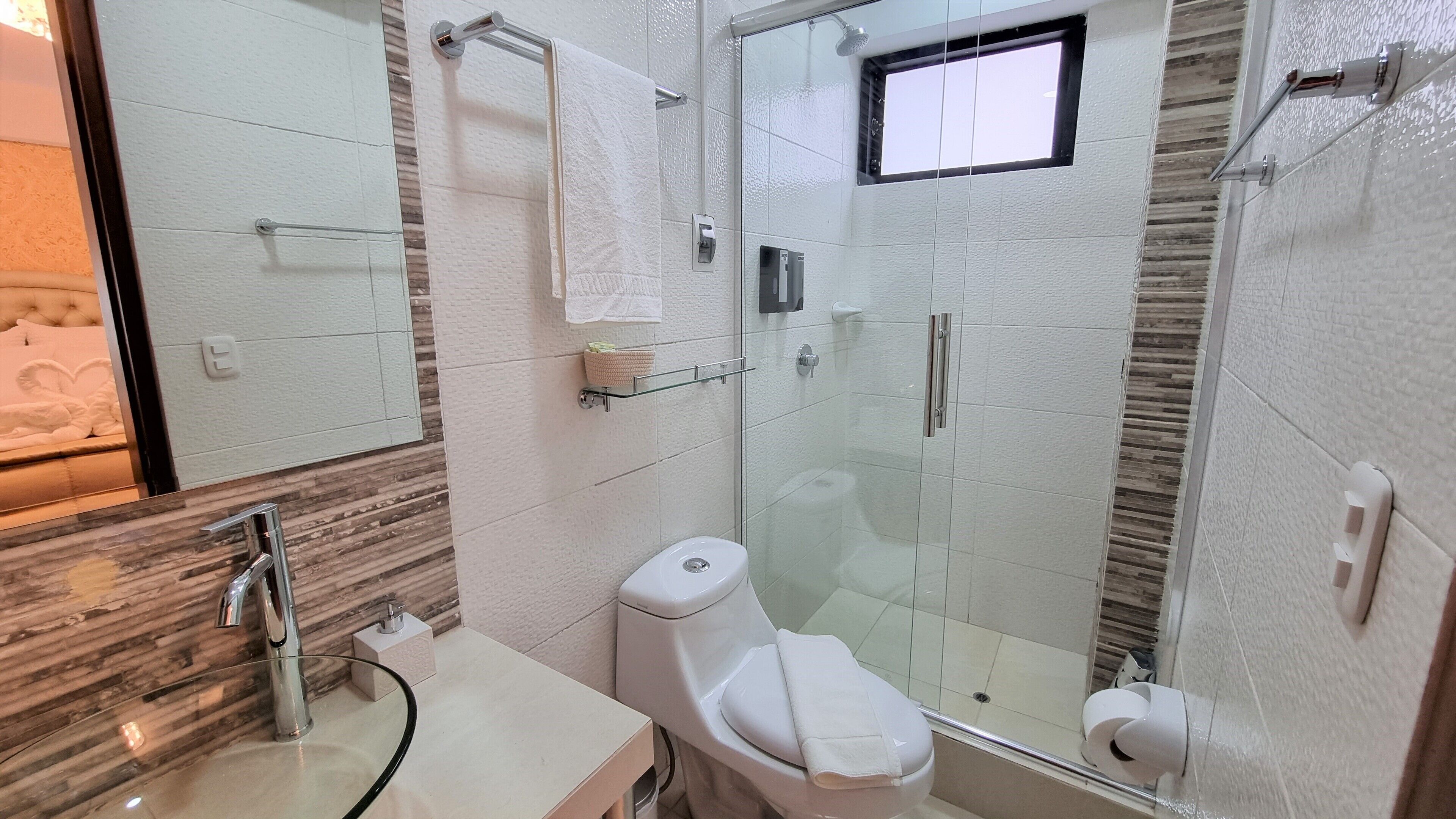 A modern bathroom with a glass shower enclosure, a toilet, and a sink with a glass countertop.