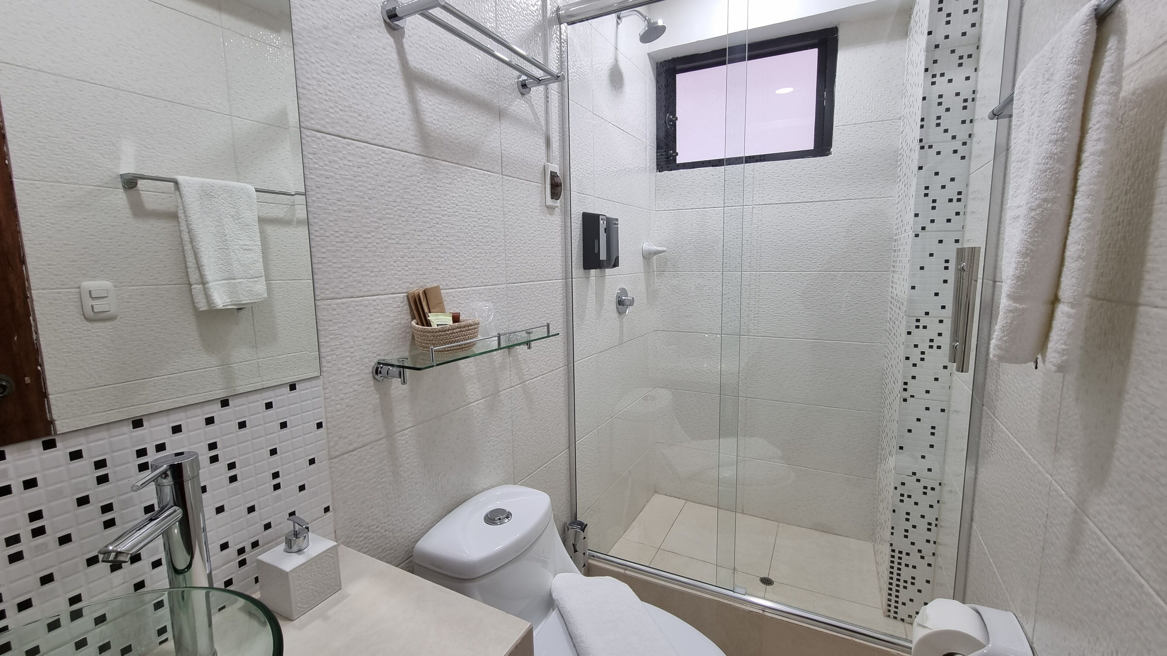 A modern bathroom with a glass-enclosed shower, white tiled walls, a glass sink, and a toilet.