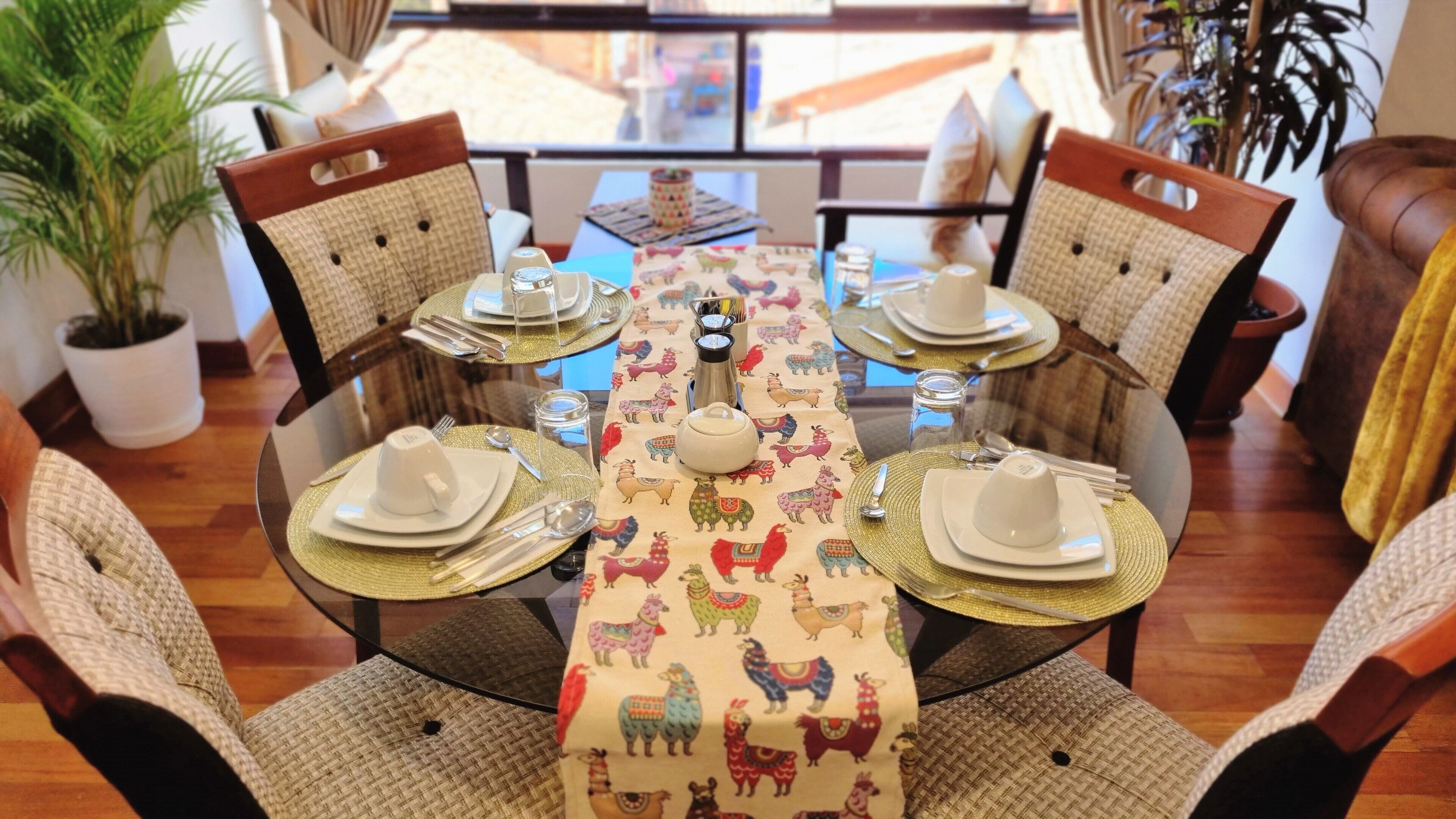 Una mesa de comedor dispuesta con platos, cubiertos y un camino de mesa decorativo con estampados de animales.