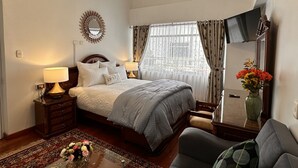 A hotel room with a bed, bedside lamps, a mirror, a TV, a sofa, and a vase with flowers. - Hotel Inkasabios Cusco (Cusco)