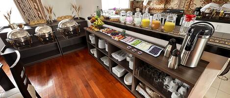 Montaje de bufé con diversos alimentos y bebidas, incluyendo frutas, pasteles y una estación de café.