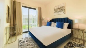 A modern bedroom with a large bed, a nightstand, a lamp, and a view of the outdoors. - SYCAMORE Damac Hills 2 {Akoya By Damac] (Downtown Dubai)