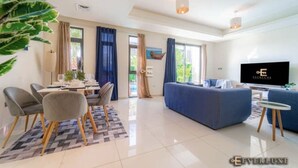 A modern living room with a sofa, TV, and dining area with chairs and a table. - SYCAMORE Damac Hills 2 {Akoya By Damac] (Downtown Dubai)