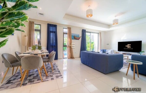 A modern living room with a sofa, TV, and dining area with chairs and a table.