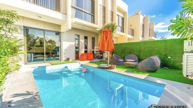 A modern pool area with a clear blue pool, outdoor seating, and a green wall. - SYCAMORE Damac Hills 2 {Akoya By Damac] (Downtown Dubai)