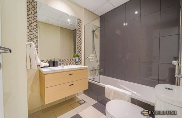 A modern bathroom with a beige vanity, a large mirror, a shower, and a toilet.