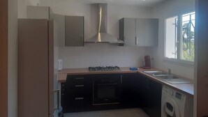 Une cuisine moderne dotée d’appareils électroménagers intégrés, notamment une cuisinière, un four et un lave-linge, ainsi qu’une fenêtre laissant entrer la lumière naturelle.