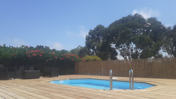 Une terrasse en bois avec une piscine, entourée d’une clôture en bois et d’une végétation luxuriante.