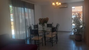 Un espace repas comprenant une table et des chaises, un lustre, une plante en pot et une vue sur l’extérieur.