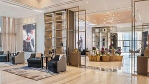 Eine moderne Hotelhalle mit großzügigem Design, einer zentralen Sitzecke mit Sofas und Sesseln, einem großen abstrakten Gemälde an der Wand und einer Glastrennwand mit Dekoration im Inneren.