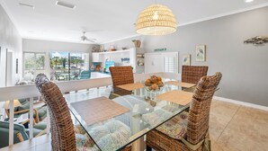 A modern dining area with a glass table, wicker chairs, and a hanging light fixture. - Our House Lake House by Beachside Mgt (Siesta Key)