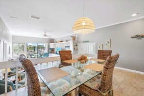 A modern dining area with a glass table, wicker chairs, and a hanging light fixture.