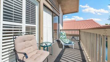 A balcony with a beige chair, a glass table, and a lounge chair with a leaf-patterned cushion.