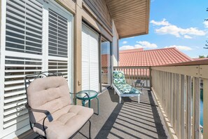 A balcony with a beige chair, a glass table, and a lounge chair with a leaf-patterned cushion. - Our House Lake House by Beachside Mgt (Siesta Key)