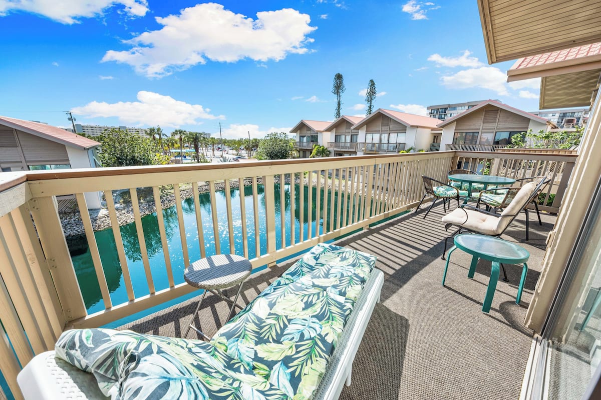 A balcony with a pool, lounge chairs, and a table.