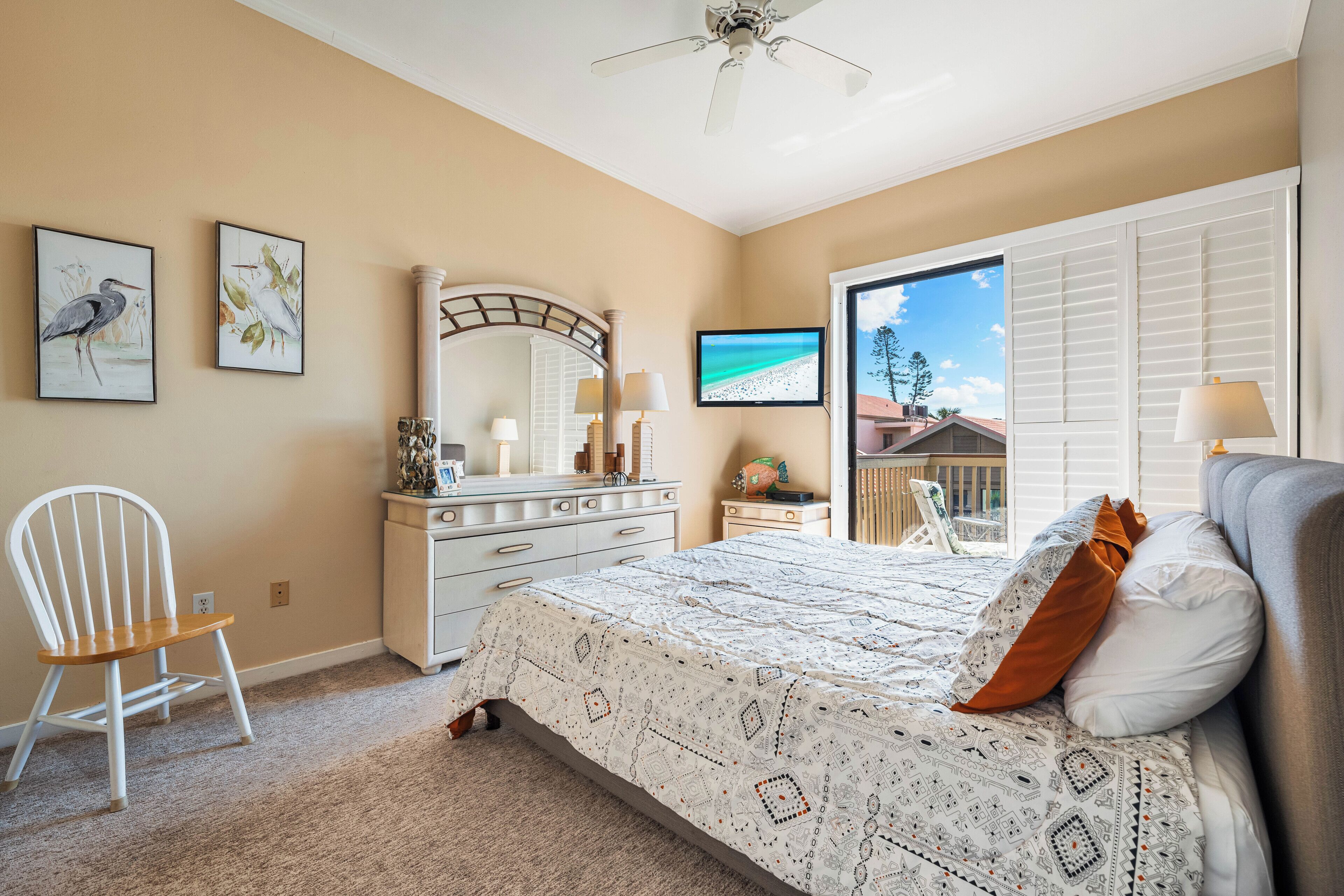 A bedroom with a bed, a chair, a dresser, a mirror, and artwork on the walls.