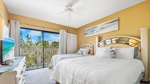 A hotel room with two beds, a ceiling fan, a large window with curtains, and a view of greenery outside. - Our House Lake House by Beachside Mgt (Siesta Key)