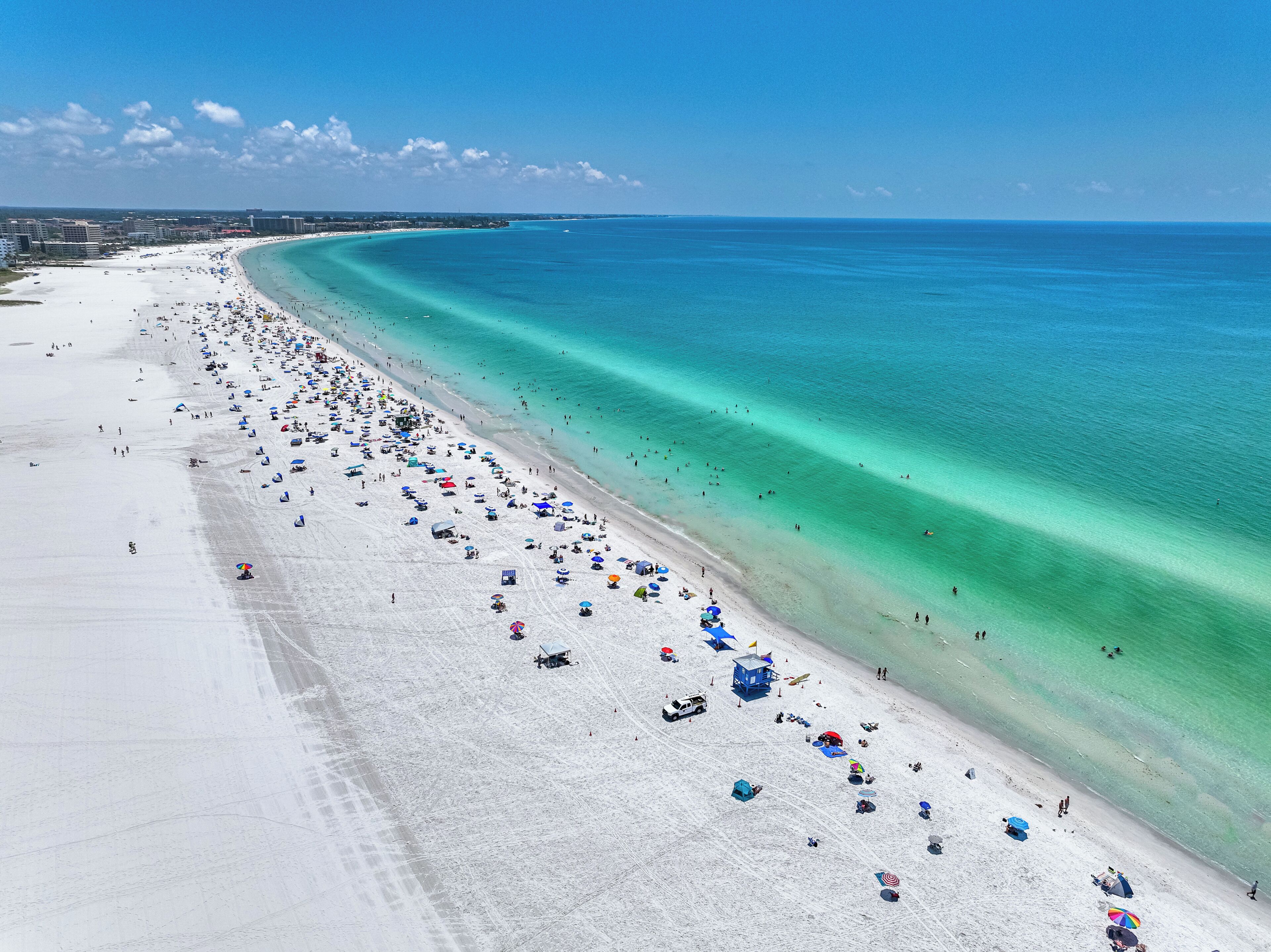 Ein weiter Sandstrand mit klarem, türkisblauem Wasser.