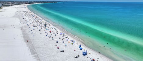A wide beach with clear turquoise waters and a long stretch of white sand.