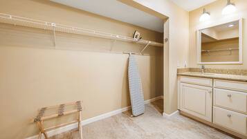 A bathroom with beige walls, a wooden drying rack, a hanging shower curtain, and a vanity with a mirror and countertop.