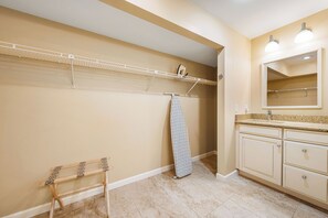 A bathroom with beige walls, a wooden drying rack, a hanging shower curtain, and a vanity with a mirror and countertop. - Our House Lake House by Beachside Mgt (Siesta Key)