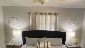 Une chambre à coucher comprenant un lit, deux tables de chevet, un ventilateur de plafond et un banc.