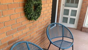 Deux chaises en osier bleu, dotées d’une structure en métal, sont placées sur une terrasse en béton, adossées à un mur de briques.