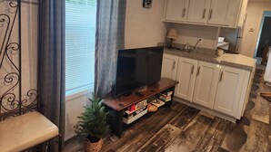 Una cocina compacta con armarios blancos, una encimera de madera, un televisor sobre un mueble y una pequeña planta en maceta.