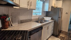 Una cocina moderna con armarios blancos, un lavamanos de acero inoxidable, lavavajillas y refrigerador.