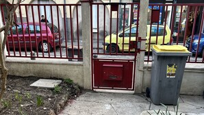 Een poort met een rode poort, een gele auto die er geparkeerd staat, en een afvalbak aan de rechterkant.