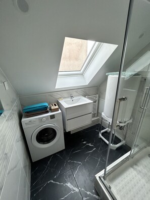 Une petite salle de bain avec un puits de lumière, un lave-linge, un évier et une douche.