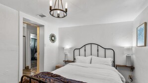Una camera da letto con un letto, lampade sui comodini, un lampadario, una porta in legno e una piccola mensola.
