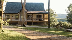 A two-story house with a covered porch, surrounded by trees and a gravel path. - Huckleberry Hollow, secluded home in the woods, wraparound porch, soaker tub! (Galena)
