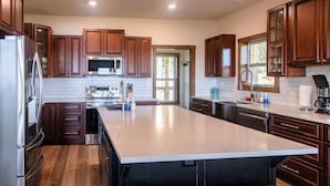A modern kitchen with wooden cabinets, stainless steel appliances, and a large island with stools. - Huckleberry Hollow, secluded home in the woods, wraparound porch, soaker tub! (Galena)