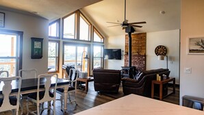 A spacious living area with a dining table, chairs, a sofa, and a television. - Huckleberry Hollow, secluded home in the woods, wraparound porch, soaker tub! (Galena)