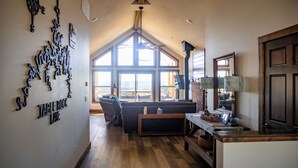 A spacious living area with a large window, a fireplace, and a cozy seating arrangement. - Huckleberry Hollow, secluded home in the woods, wraparound porch, soaker tub! (Galena)