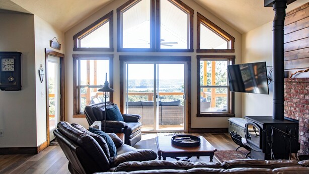A spacious living room with a large window, a fireplace, and a television. - Huckleberry Hollow, secluded home in the woods, wraparound porch, soaker tub! (Galena)