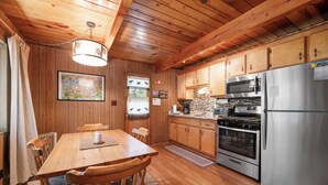 Una cocina con paneles de madera, una mesa de comedor, sillas, un refrigerador, una estufa y un microondas.