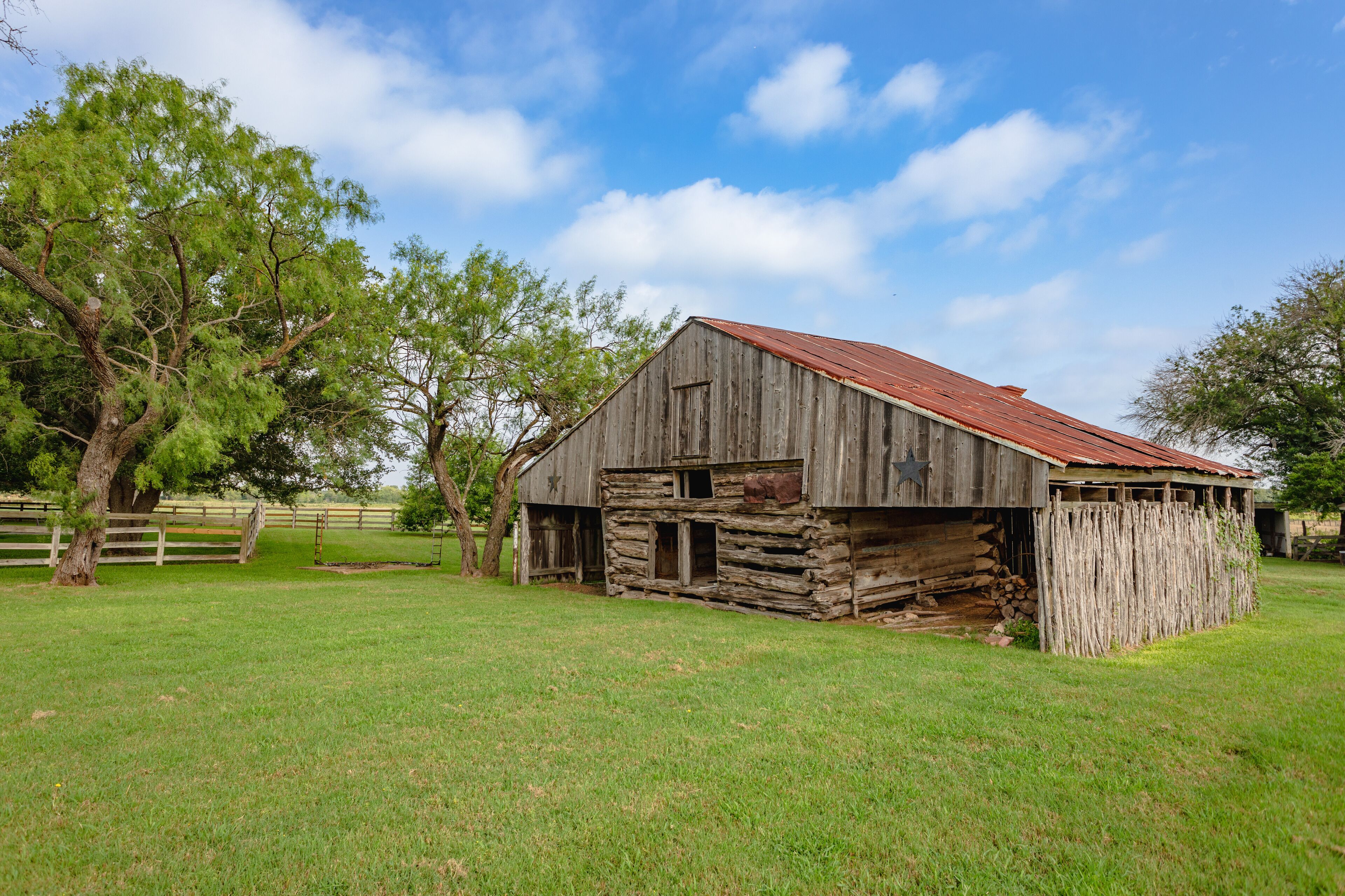 A rustic wooden barn with a red roof, surrounded by a grassy field and trees.