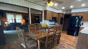 A spacious kitchen with wooden flooring, a dining table with chairs, wooden cabinets, and a black refrigerator. - Mountain Cabin ATV trails, convenient and comfort. Enjoy nature Lots of parking (Young)