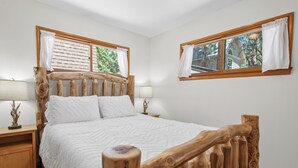 Una camera da letto con testiera in legno, un letto con biancheria bianca, due comodini con lampade e finestre con tende.
