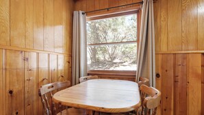 Un interno in legno con un tavolo rotondo e sei sedie, una finestra con tende e vista sugli alberi.